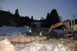 崩落斜面から流れてきた泥と水の流路を確保するため土のうを置く作業員ら=27日午後6時半すぎ