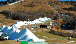 黒っぽい造雪機(右)からパイプで送られた人工雪が次々と白い山になっていく=九重町湯坪