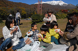 大山の紅葉と冠雪を背にバーガーを頬張る家族連れ=3日、江府町御机の奥大山スキー場