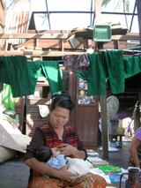 ビルマの現状、屋根の無い家の中で乳飲み子を抱く母