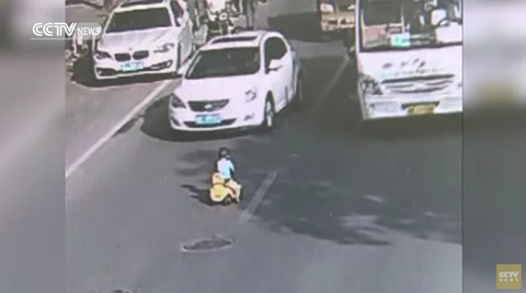 Kid drives toy car through traffic on busy road
