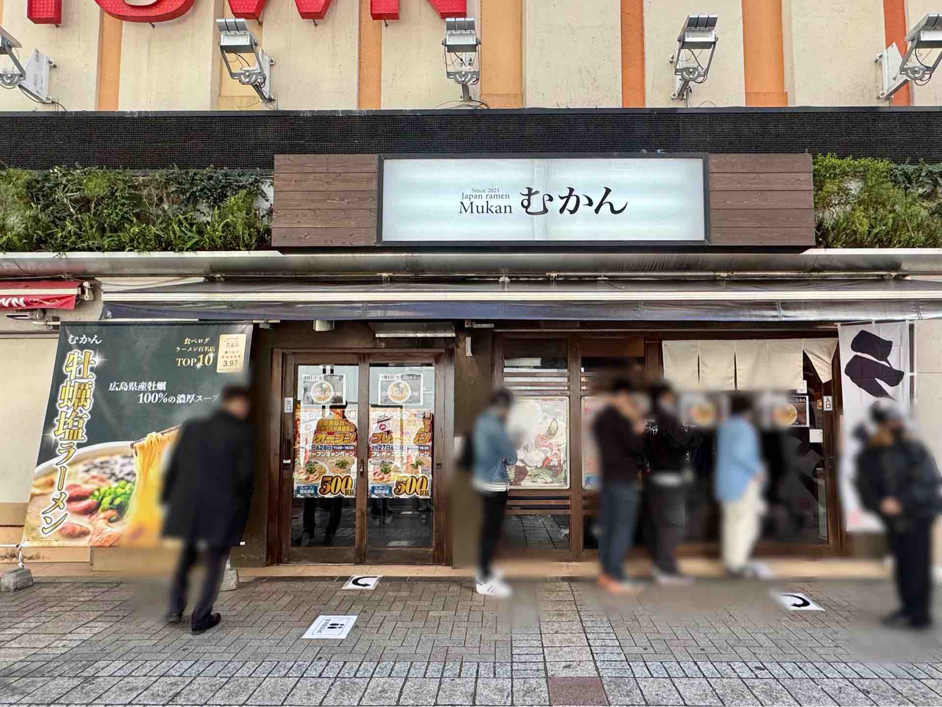 2026年池袋に新しくオープンしたラーメン店の外観、モダンで洗練されたデザインの店舗ファサード、看板に「むかん」と書かれた文字、昼間の明るい雰囲気、リアルな写真風イラスト