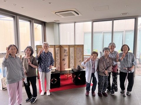 複数の入居者が室内で立ち並び、屏風の前で集合写真を撮っている様子