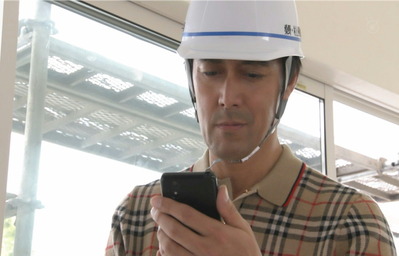 建築現場でヨガのインストラクターのプロフィールを見ている桑野