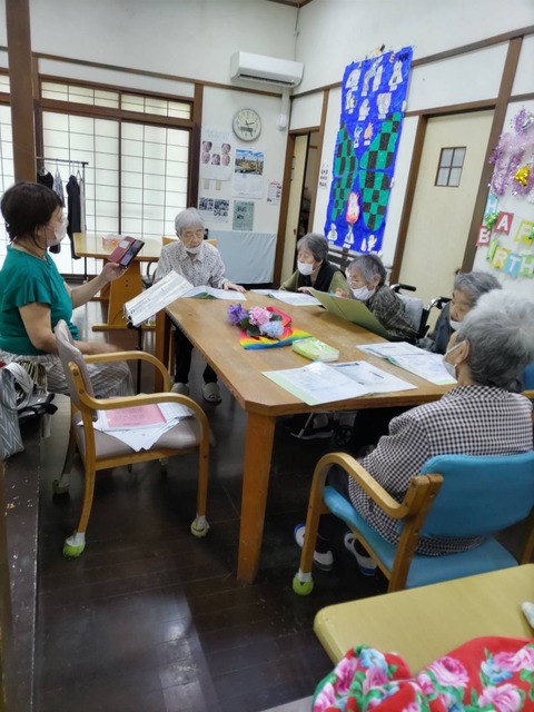 介護施設の共用室でレクリエーション活動を行う高齢者と職員。創作活動や交流の場面。