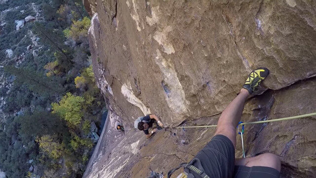 命綱なしで垂直の岩壁を登るクライマーを通過待ちするクライマー