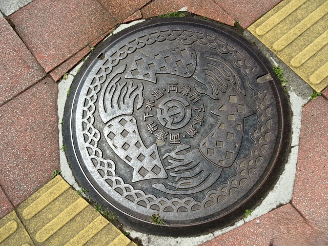 現佐渡市、旧両津市下水。特産のイカをデザインし中央に市章と下水道の文字