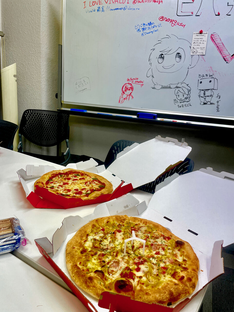 当日食べたピザの写真とホワイトボード。机の上にピザが2つ。奥のホワイトボードにはトニーのイラスト。