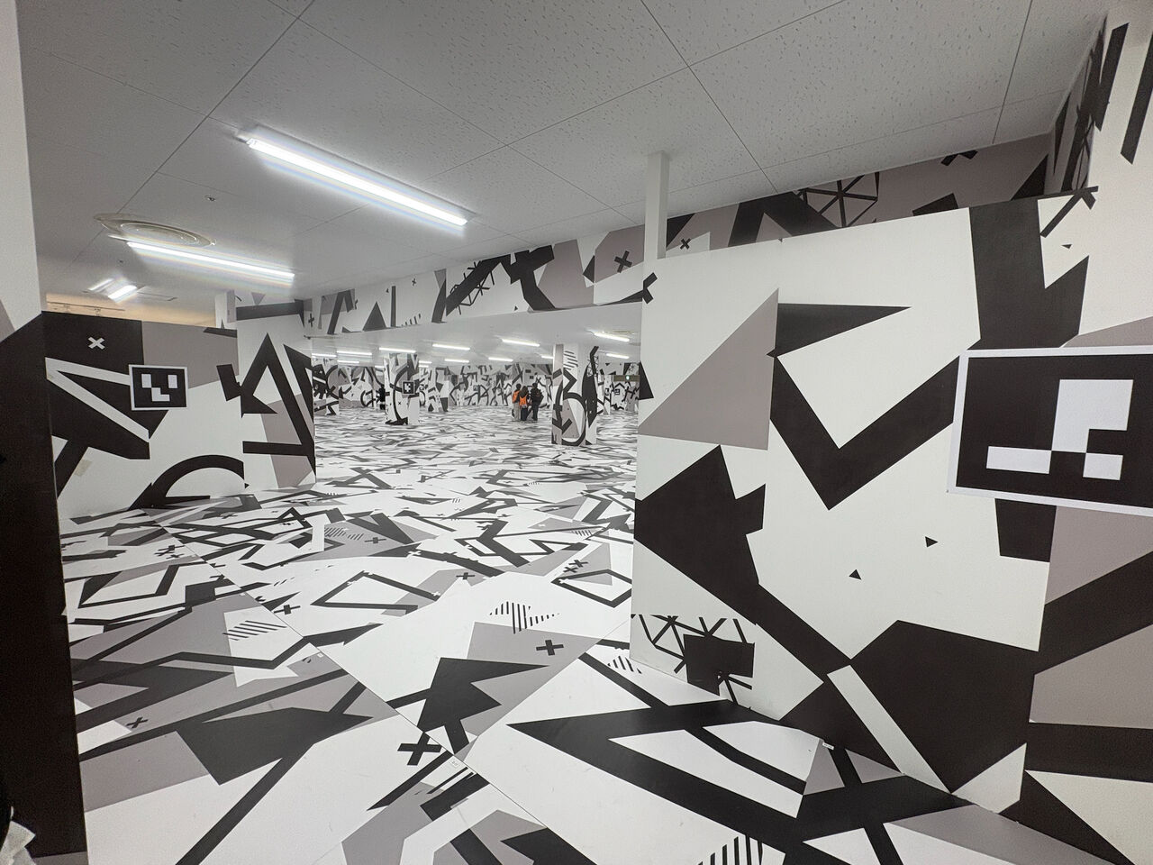 イマーシブジャーニーの体験スペース、広い何も無いスペースに柱や壁だけがある、柱や壁・天井は白地に黒い奇天烈な模様がつけられてる