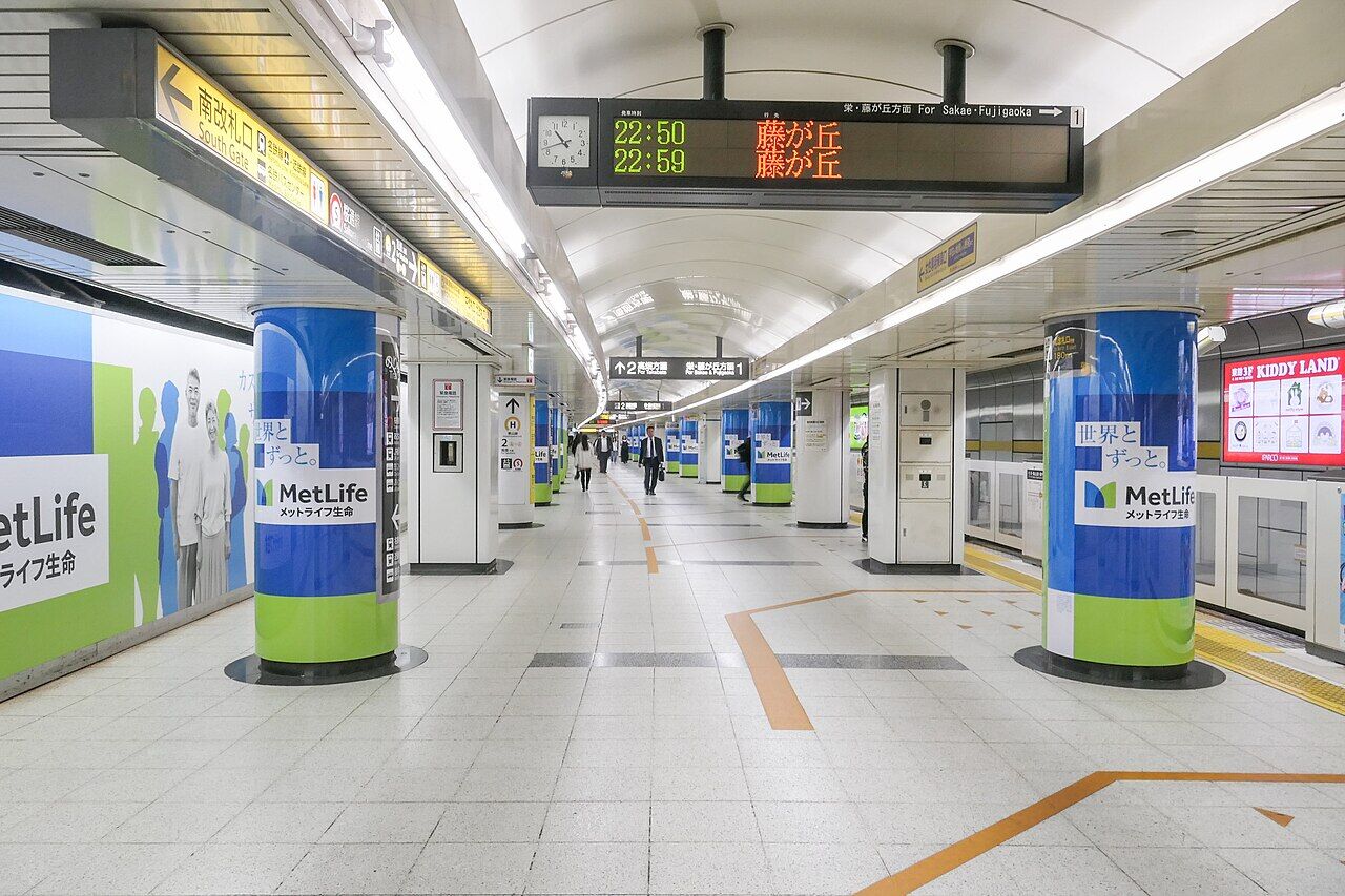 地下鉄東山線の名古屋駅のホーム、左側は壁に緑と青色の広告、右側はホームドアが設置されてる。