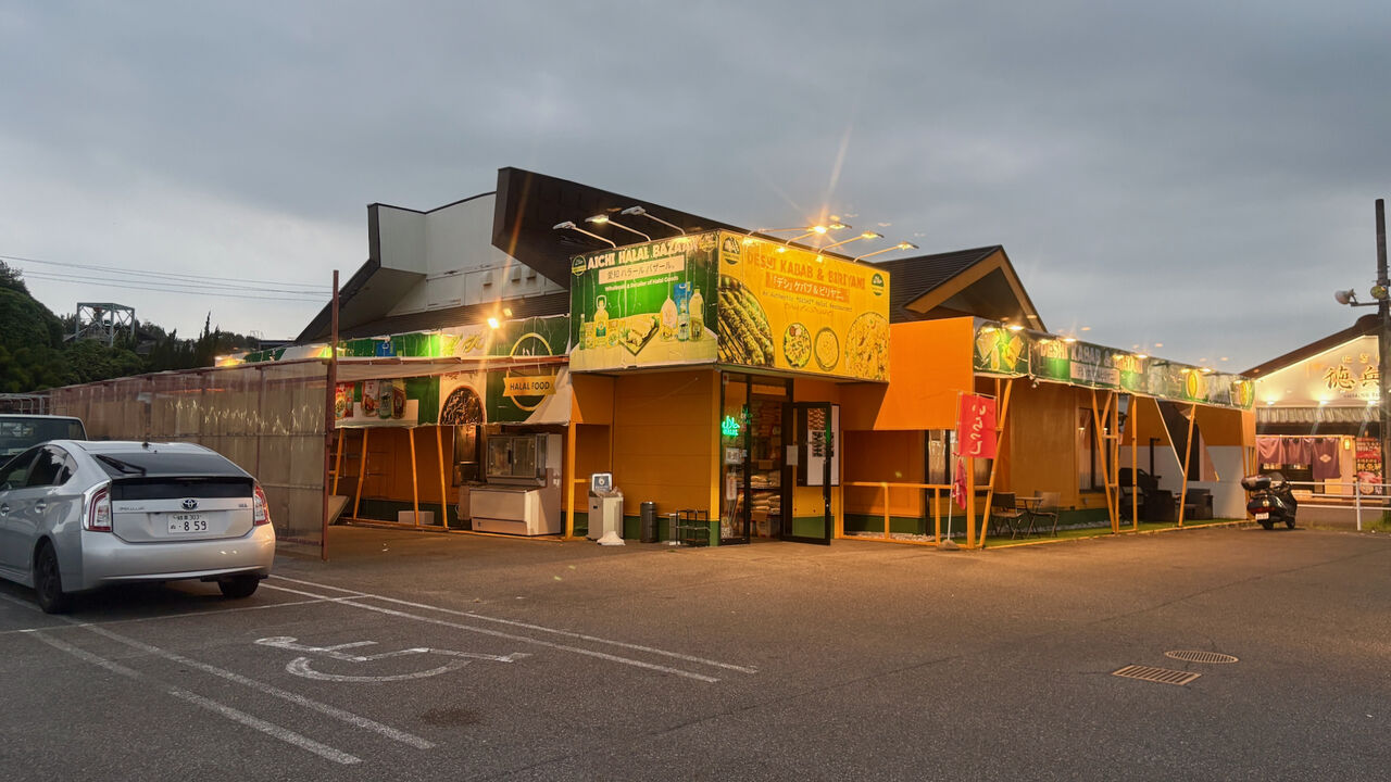 夕暮れ時の店舗外観、建物は黄色基調で緑色の装飾といった感じ