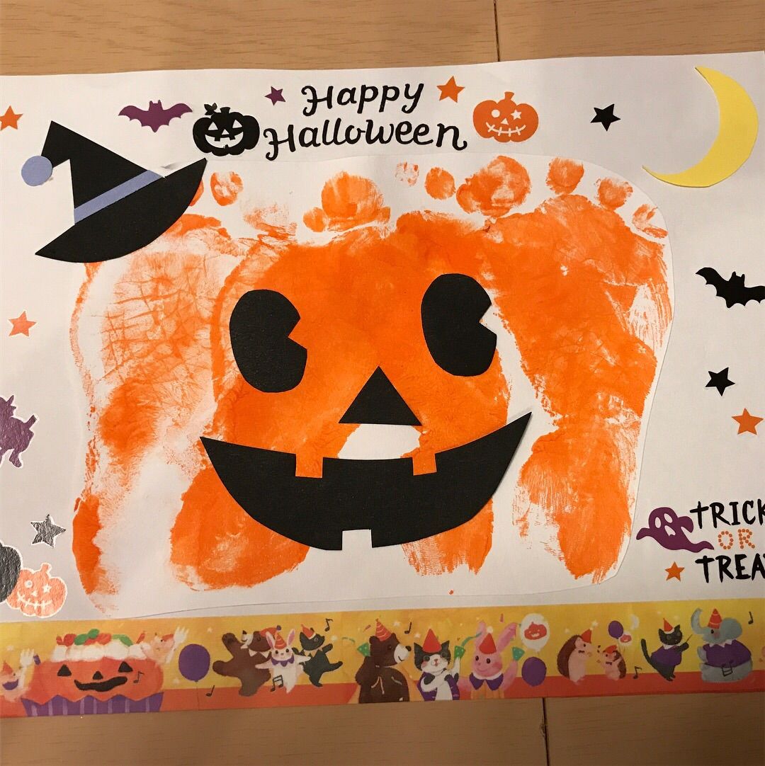 A charming baby handprint art project for Halloween, featuring tiny orange and black handprints shaped like pumpkins and ghosts, made by a one-year-old and six-month-old baby