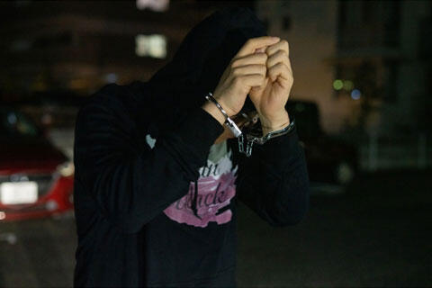 手錠された手で顔を隠す犯罪者　イメージ