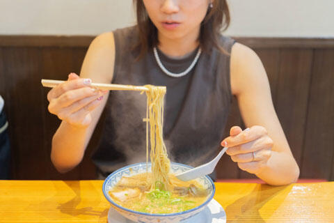 熱々のラーメンを食べる女性　イメージ