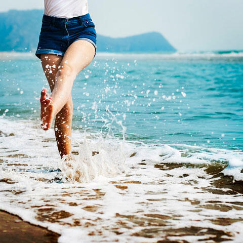 波打ち際で海水を蹴り上げる女性の足