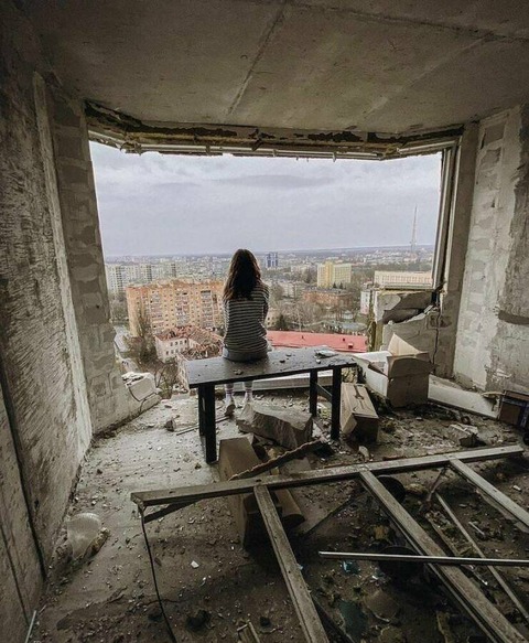 ぶっ壊されたビルの高層階に座る女性