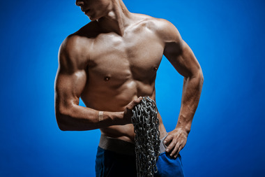 muscular-guy-with-chains-on-his-shoulders-against-a-blue-wall