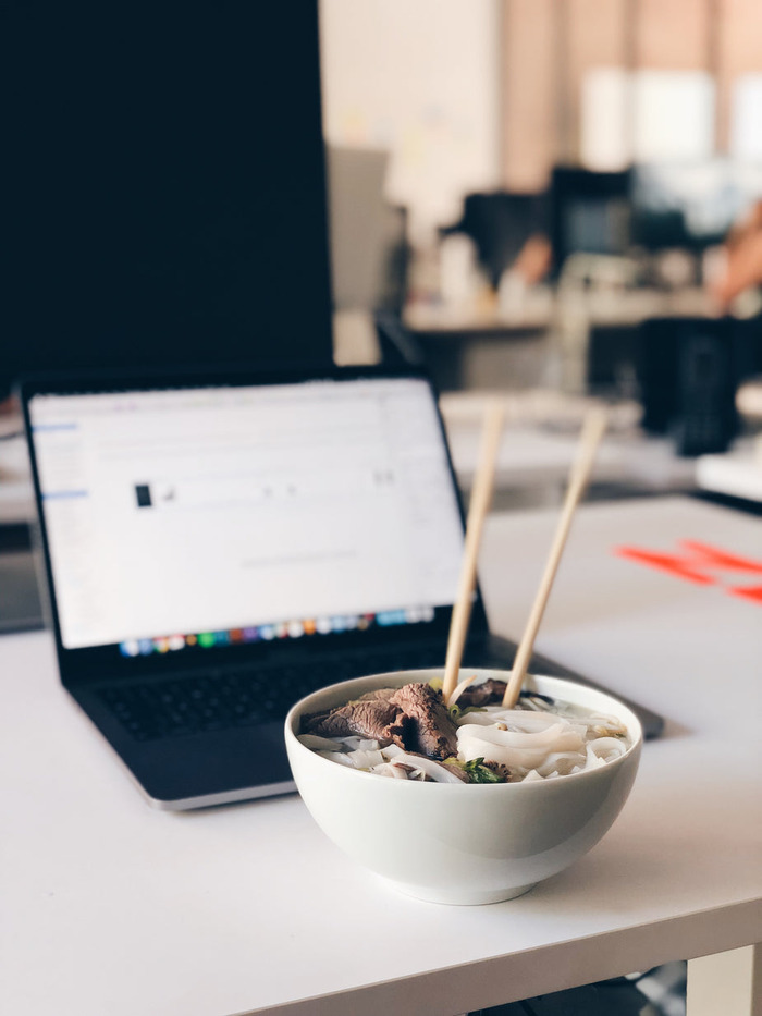 a-bowl-of-noodles-sits-in-front-of-a-laptop-on-a-desk
