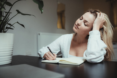 woman-closes-her-eyes-while-journalling-in-a-notebook