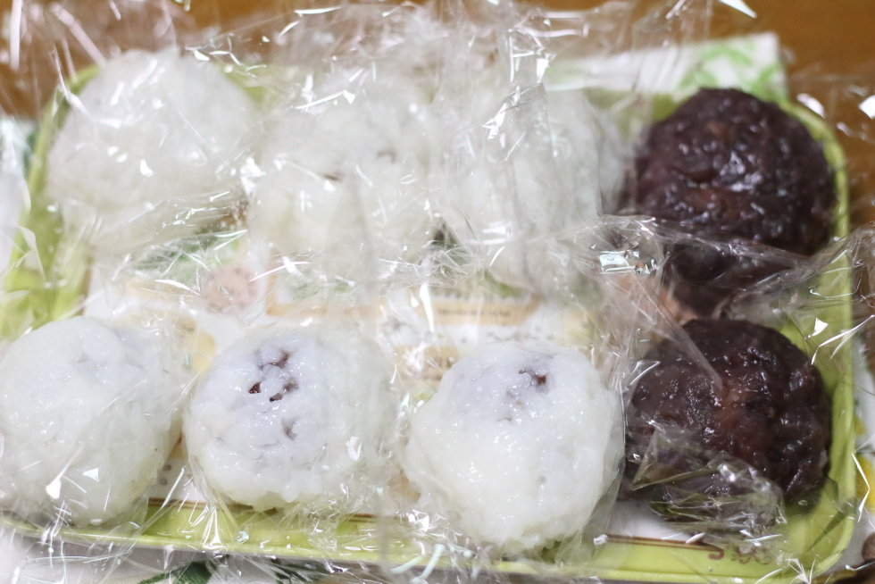透明なラップで一つずつ丁寧に包まれた、粒あん、きなこ、青のりの3種類のおはぎが複数並べられている様子。 青のりやきな粉をまぶす直前