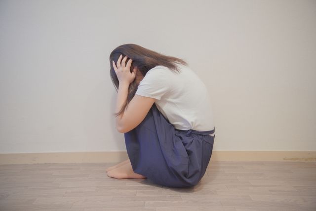 頭を押さえ膝を抱え込んで泣く女性