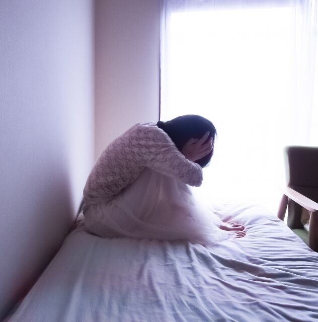 ベッドの上で頭を抱え込む少女