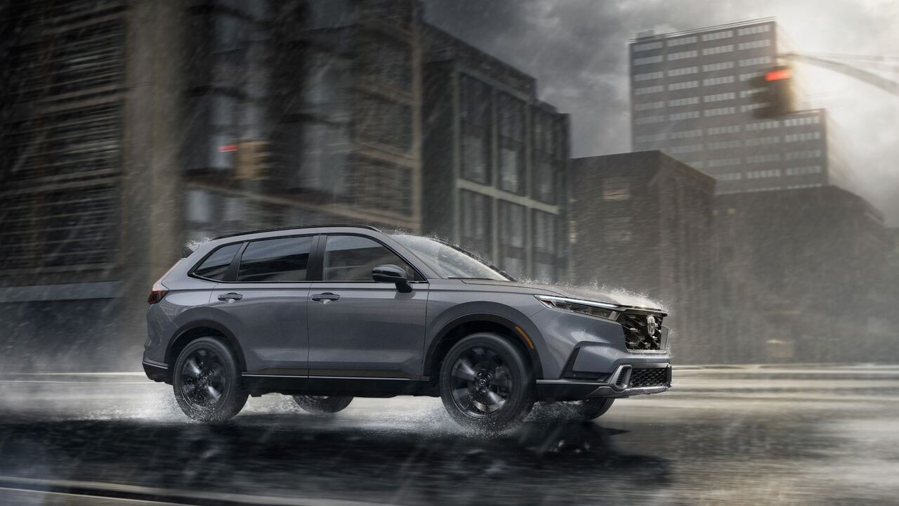 雨の街を走行するグレーの 2026 年型ホンダ CR-V スポーツ ツーリング ハイブリッドのダイナミックなフロント 3/4 ショット。