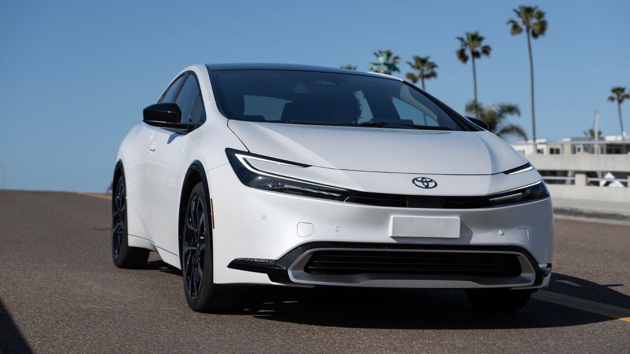 橋の上を走行する白い 2025 トヨタ プリウス PHEV XSE のダイナミックなフロント 3/4 ショット。