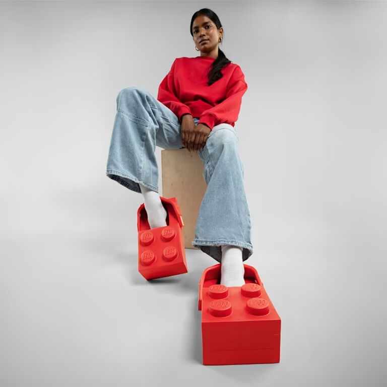 빨간색 레고 테마의 크록스, 가벼운 워시진, 빨간색 스웨트셔츠를 입은 사람이 나무 블록 위에 앉아 있습니다.