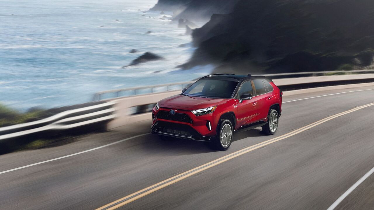 海沿いの道路を走行する赤い 2024 トヨタ RAV4 Prime XSE のダイナミックなフロント 3/4 ショット。