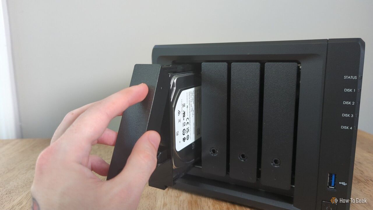 Synology DS425+ NAS のドライブ ベイ内にドライブを配置する人の手。-2