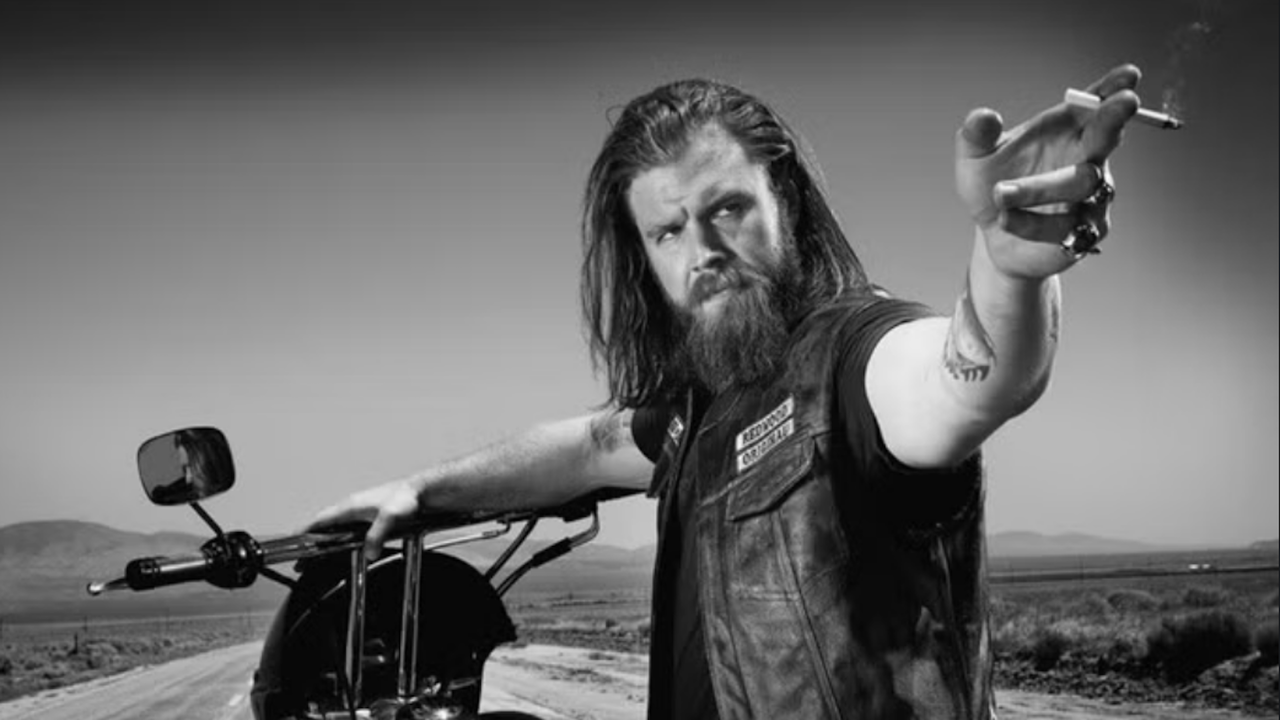 『サンズ・オブ・アナーキー』より、オピー・ウィンストン役のライアン・ハーストが彼のカラーの服を着てタバコを持って指差している白黒画像。