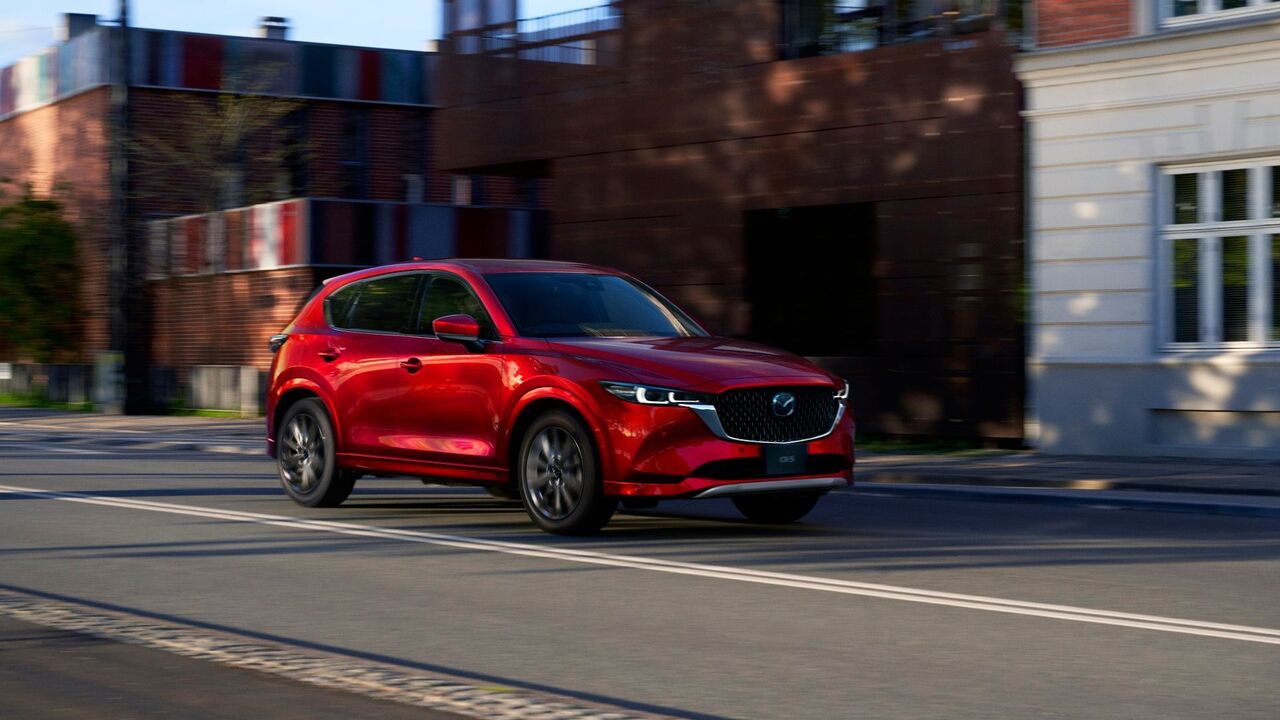 街中を走行する赤い 2025 型マツダ CX-5 の 4 分の 3 からの眺め。