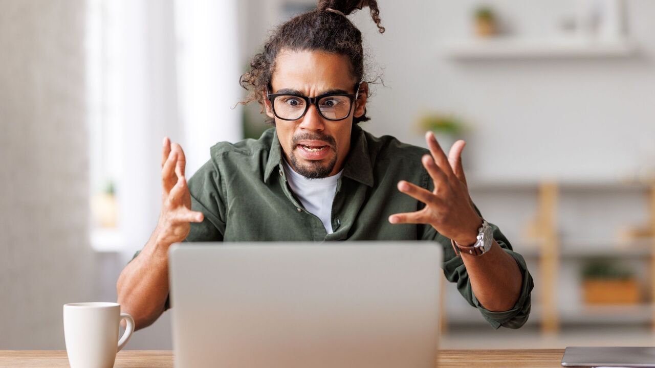 ラップトップに向かってイライラして両手を空中に投げ出す男性。