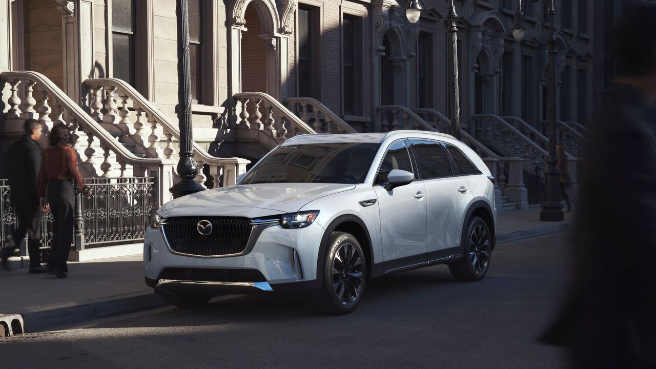 いくつかの家の外の路上に駐車された白い2026年型マツダCX-90の静的なフロント3/4ショット。