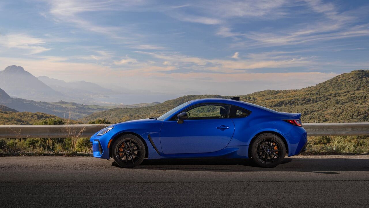 山と木々を背景にした青い 2024 型スバル BRZ tS の静的な横顔ショット。