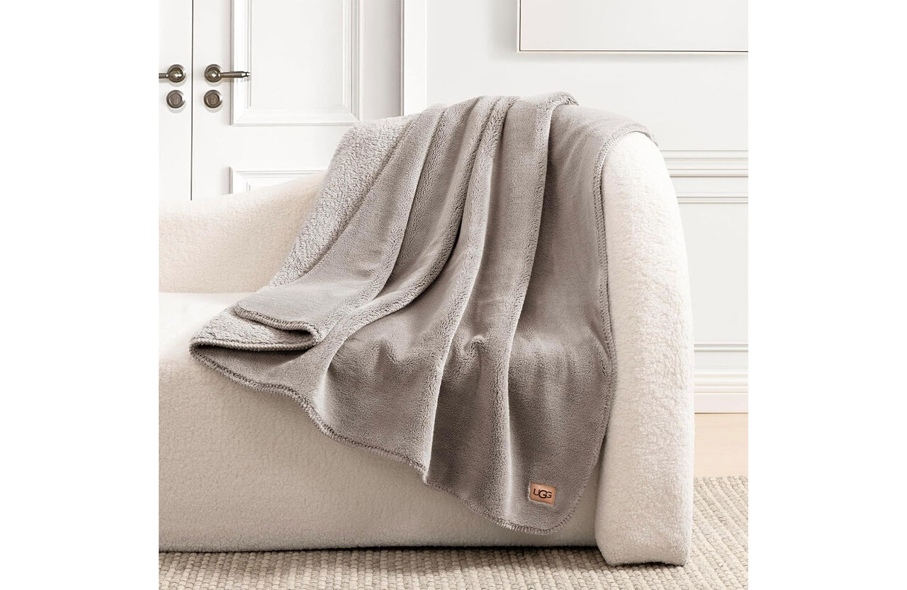 질감이 있는 베이지색 안락의자 위에 연한 회색 UGG 담요가 드리워져 있습니다.