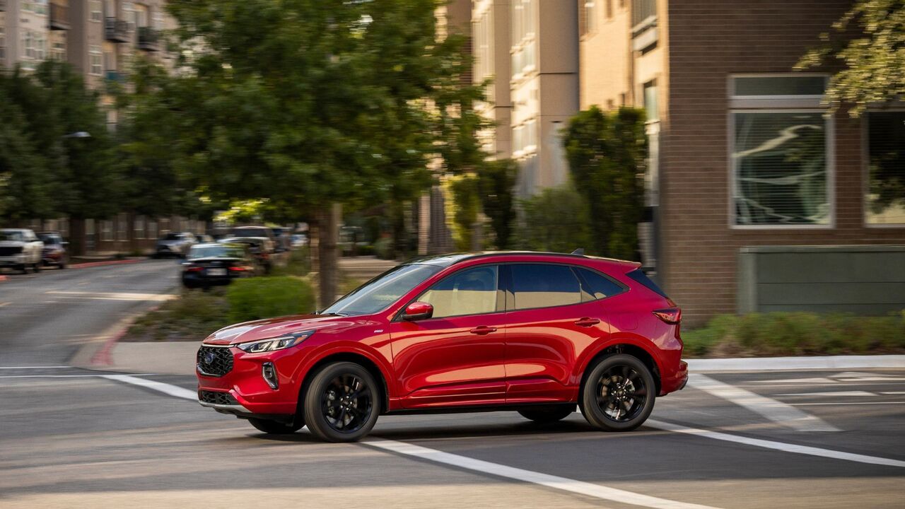 街中を走行する赤い 2023 Ford Escape ST-Line Elite のダイナミックな横顔のショット。