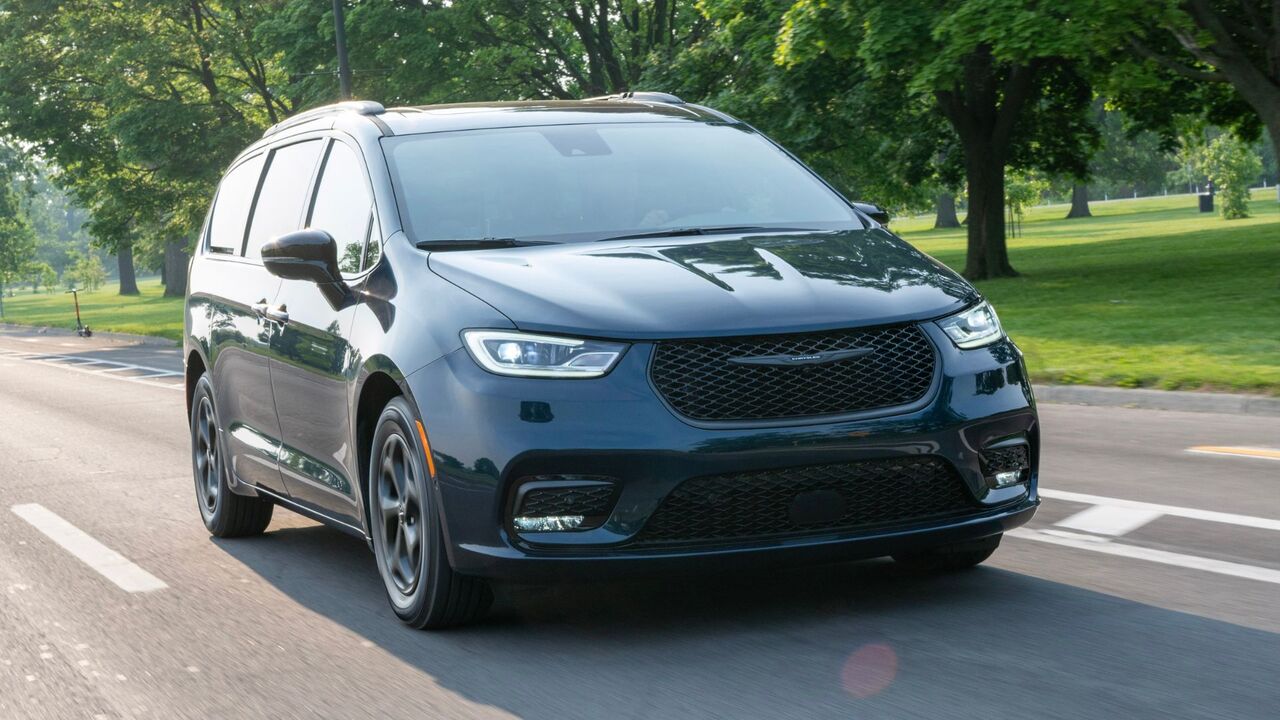 草や木々を背景に都市を走行する黒い 2025 年型クライスラー パシフィカ プラグイン ハイブリッドのダイナミックなフロント 3/4 ショット。