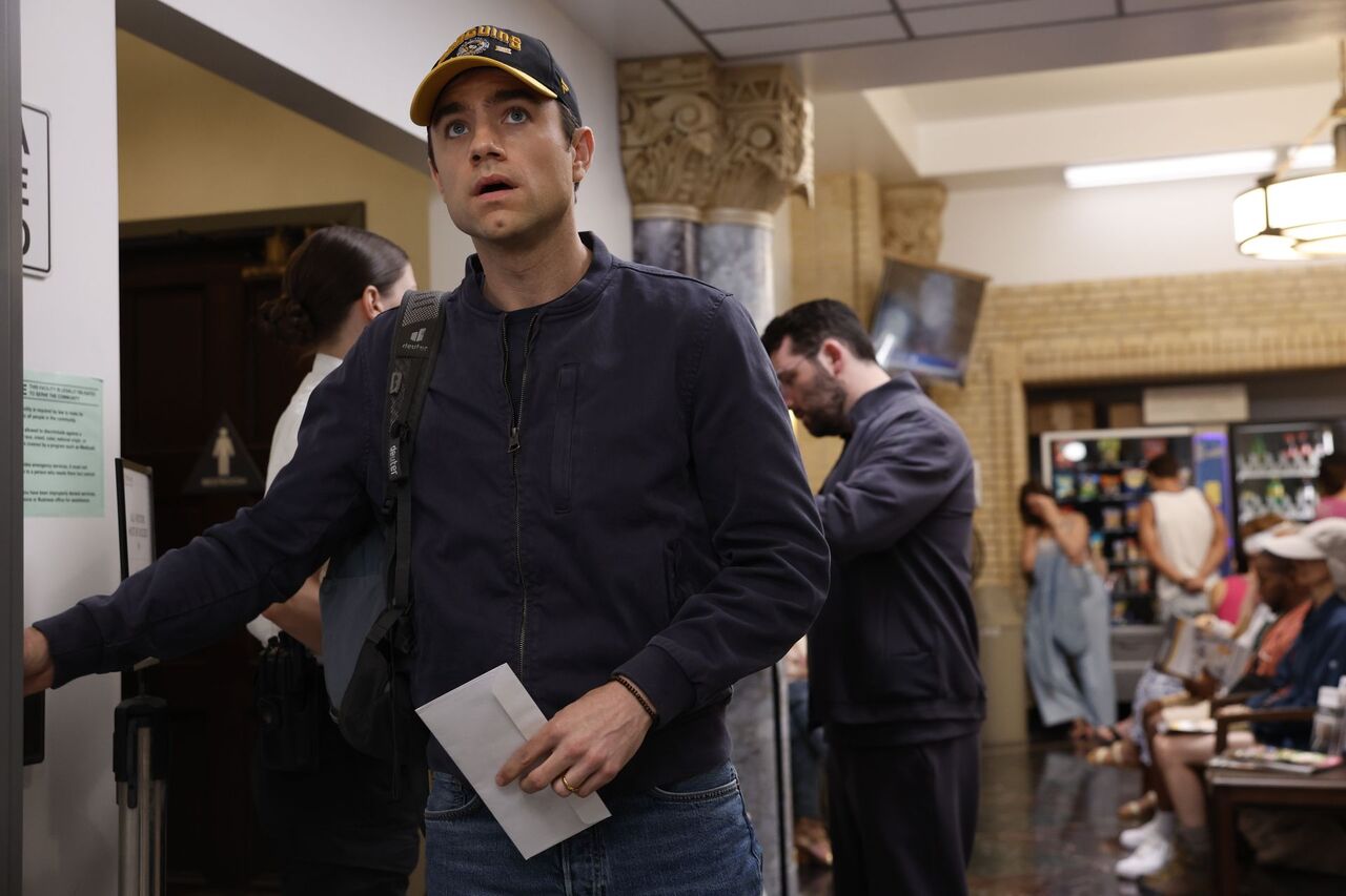 帽子とジャケットを着てバックパックを背負って仕事に戻るラングドン博士を演じるパトリック・ボール。