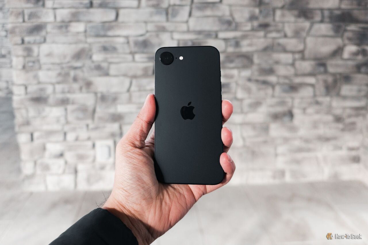 灰色の壁にiPhone 16eを手に。