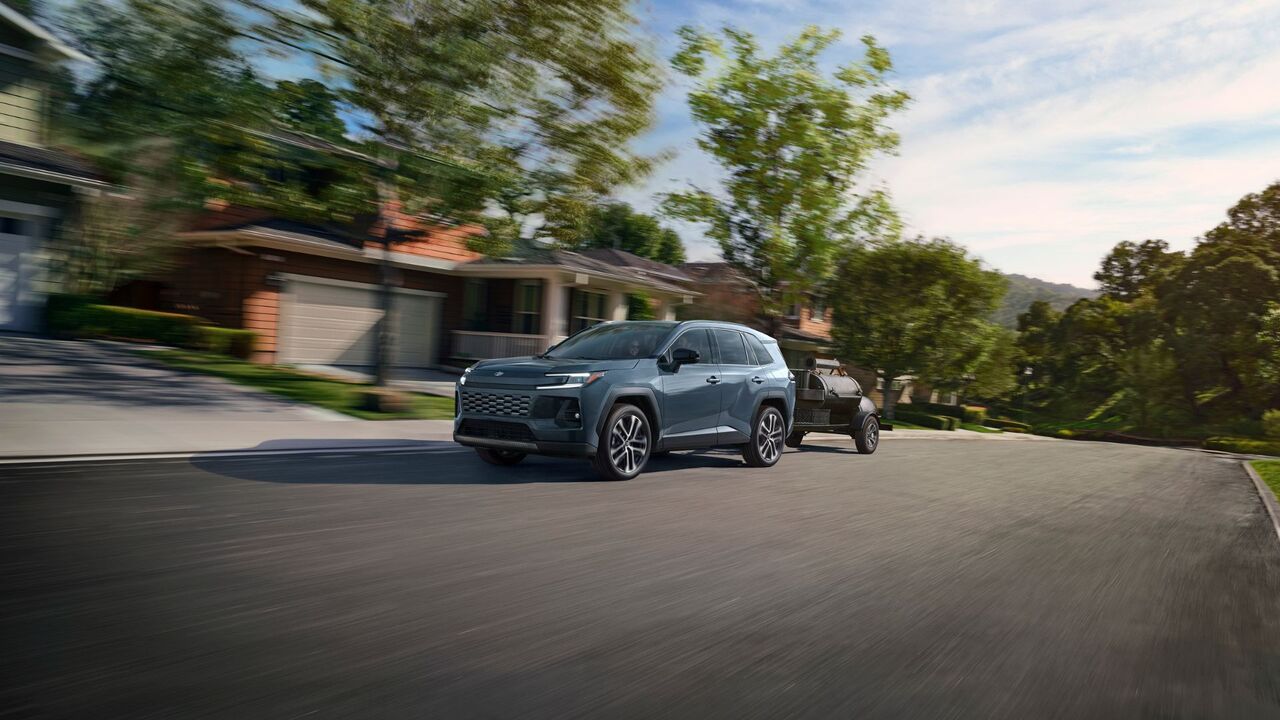 住宅街をトレーラーを牽引する青い 2026 トヨタ RAV4 リミテッドのダイナミックなフロント 3/4 ショット。