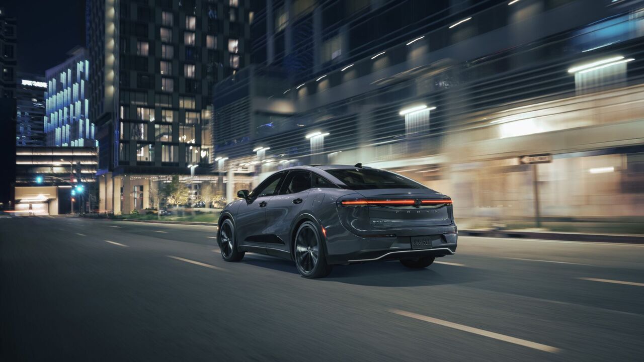 夜間に都市を走行するグレーの 2026 トヨタ クラウン ナイトシェードのダイナミックなリア 3/4 ショット。