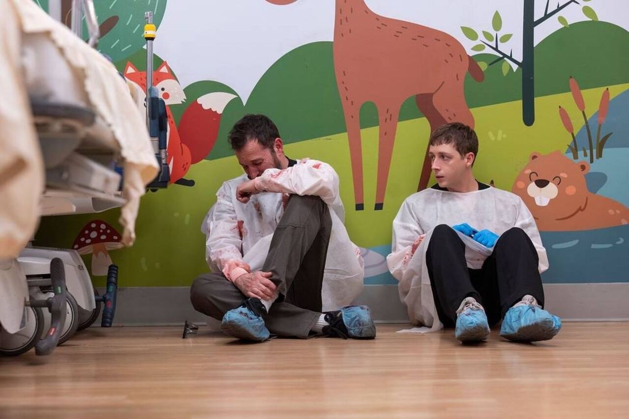 小児病室で血まみれのスクラブを着て床に座るノア・ワイリーとジェラン・ハウエル。