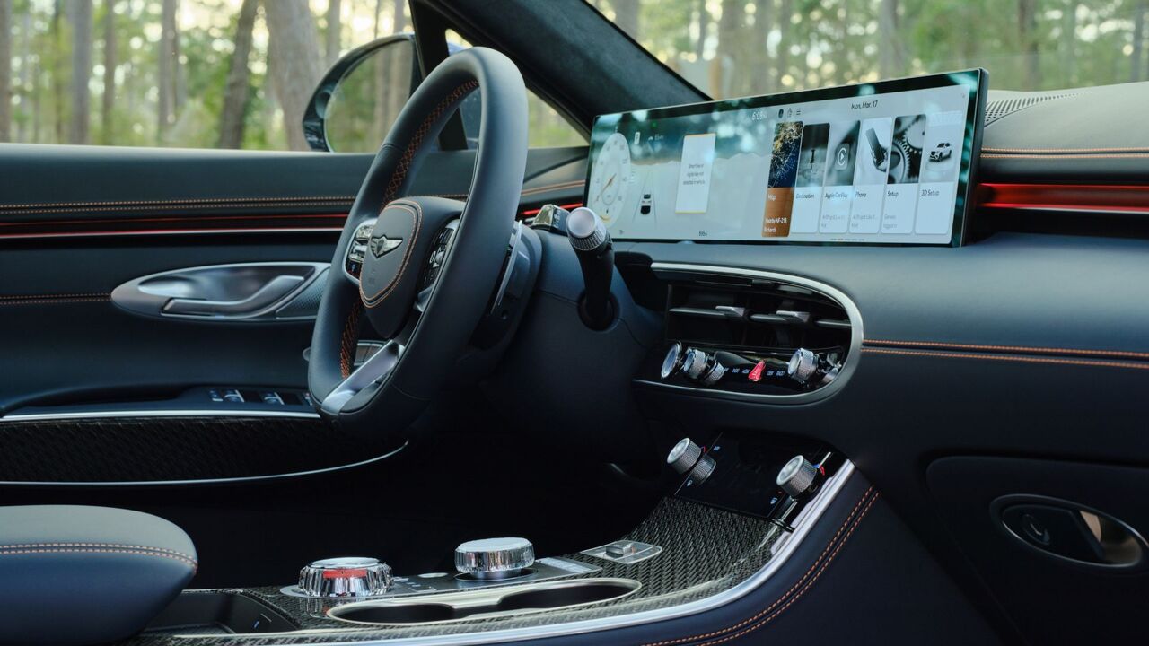 2026 年型ジェネシス GV70 のキャビン内のステアリング ホイールとインフォテインメント スクリーンのクローズ アップ ショット。