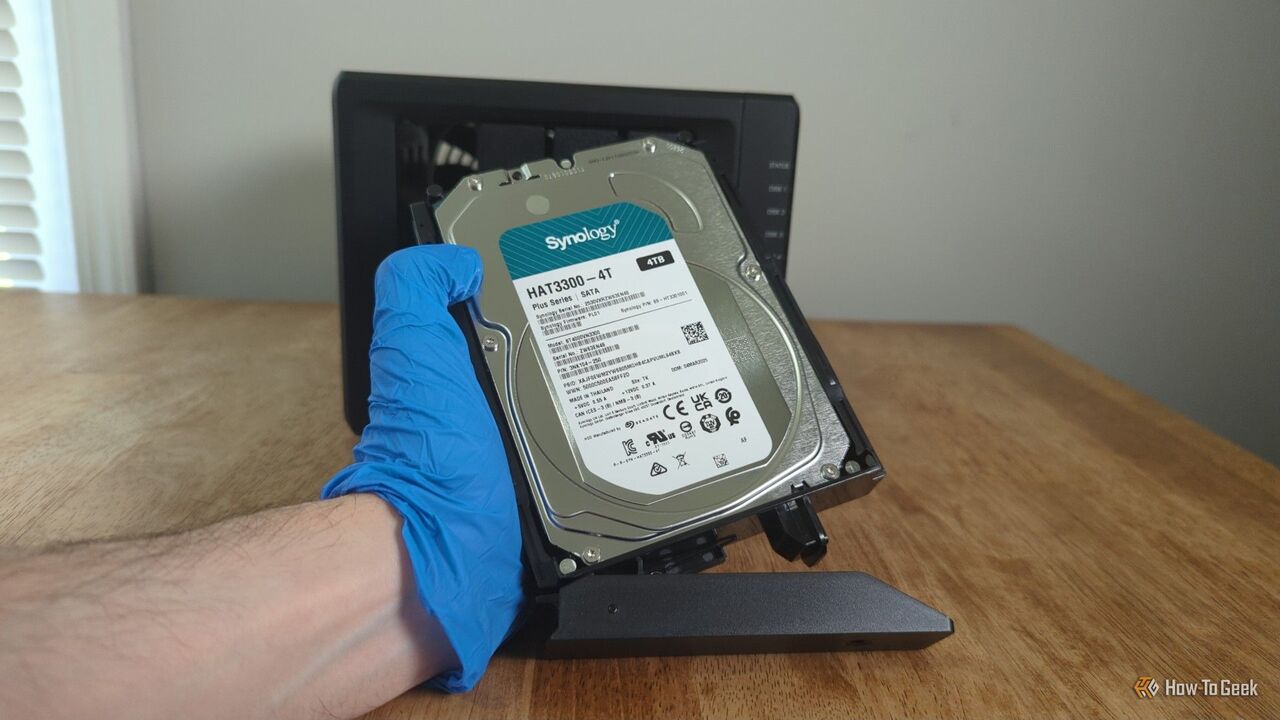 Synology DS425+ NAS の前で Synology HDD を持っている人の手袋をした手。-2