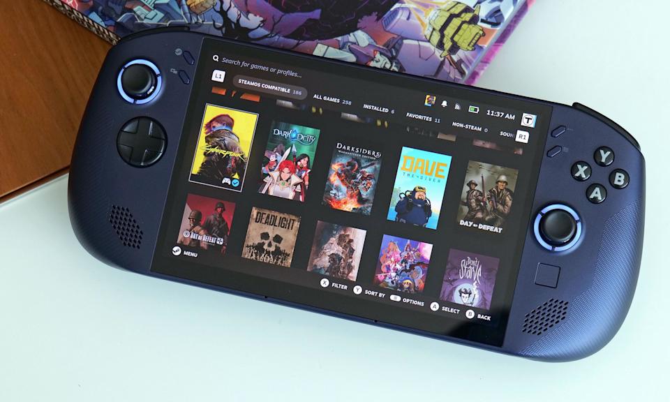 Lenovo Legion Go S는 만화책이 뒤에 있는 불투명 유리 테이블 위에 놓여 있습니다.