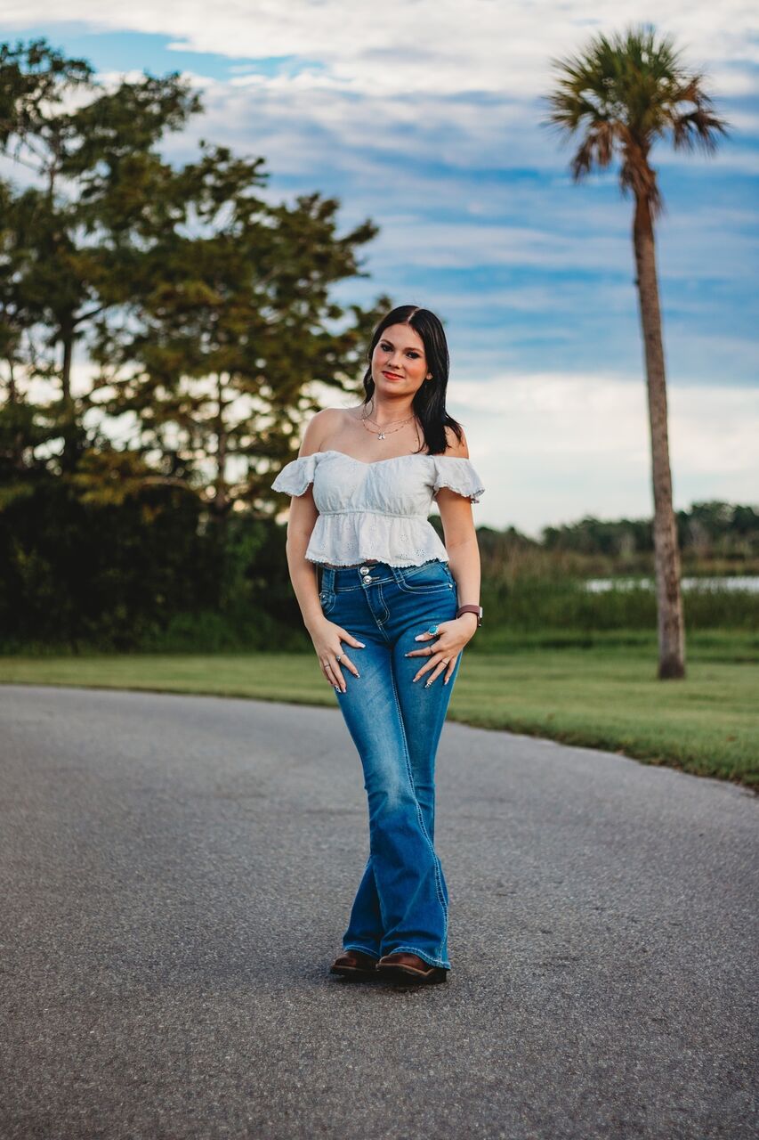 나무와 물을 배경으로 포장도로에 서 있는 안나 케프너(Anna Kepner).