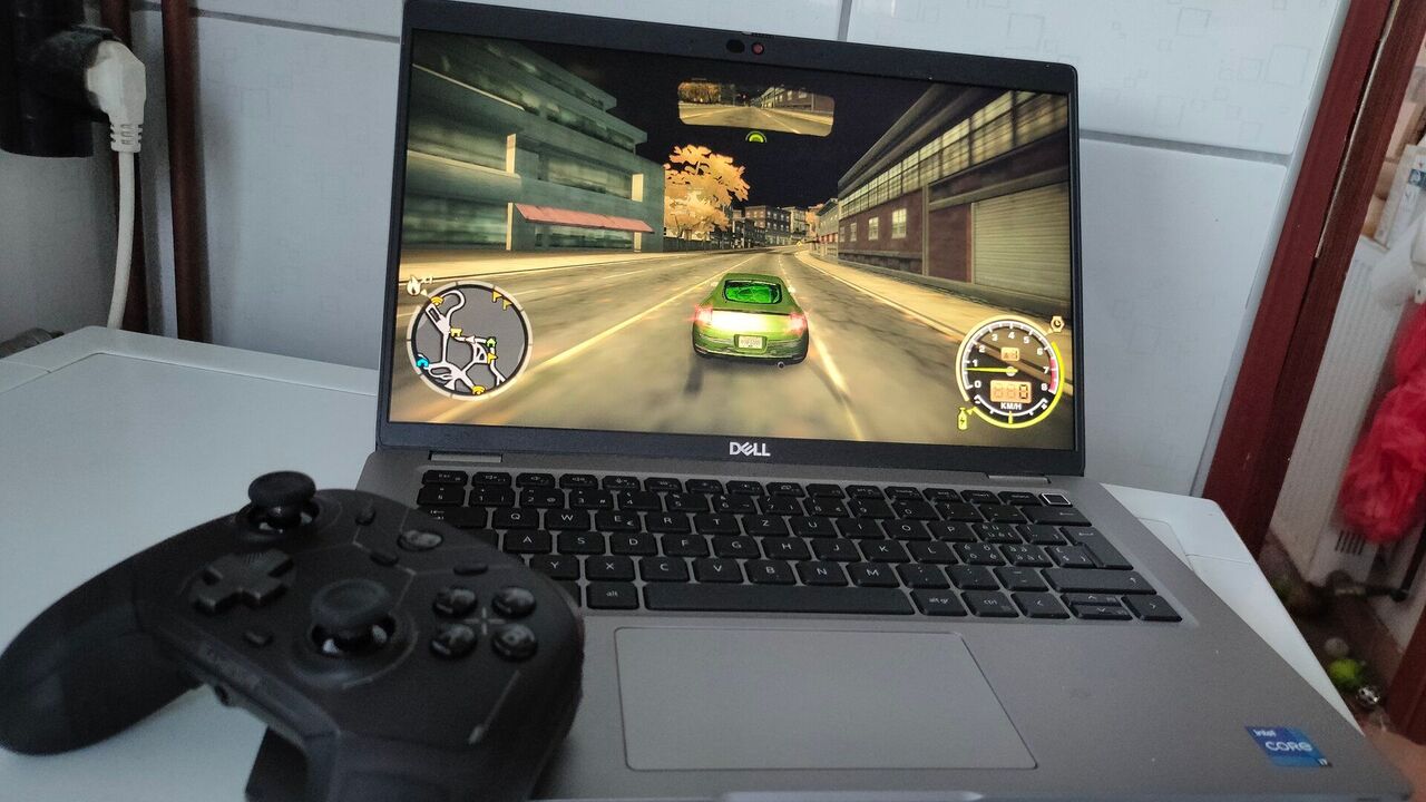 Dell Latitude 5420 ビジネス ノートパソコンが動作している "ニード・フォー・スピード モスト・ウォンテッド" キーボードの上に黒いコントローラーが付いています。