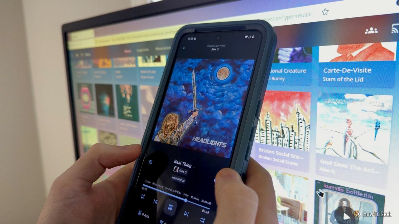 コンピューター画面の前で、Finamp アプリがインストールされた Android 携帯電話を持っている人の手。